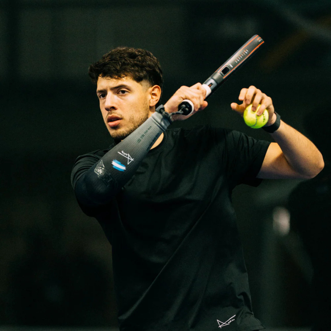 Person holding a padel racket and ball against a dark background