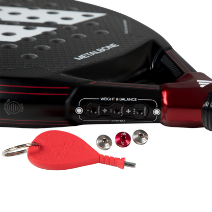 Close-up of a paddle with weight adjustment tools and a red keychain on a white background