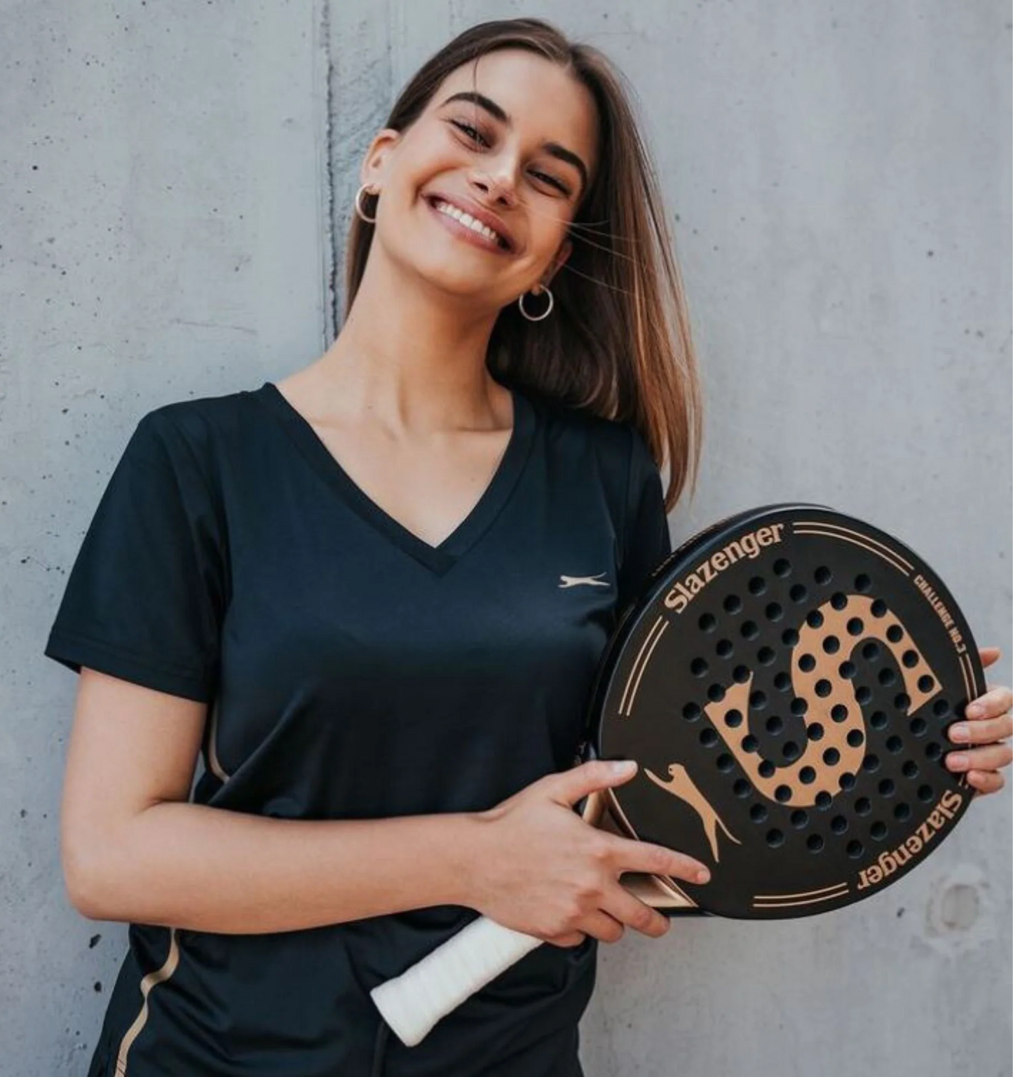Woman holding a Slazenger paddle against a concrete wall