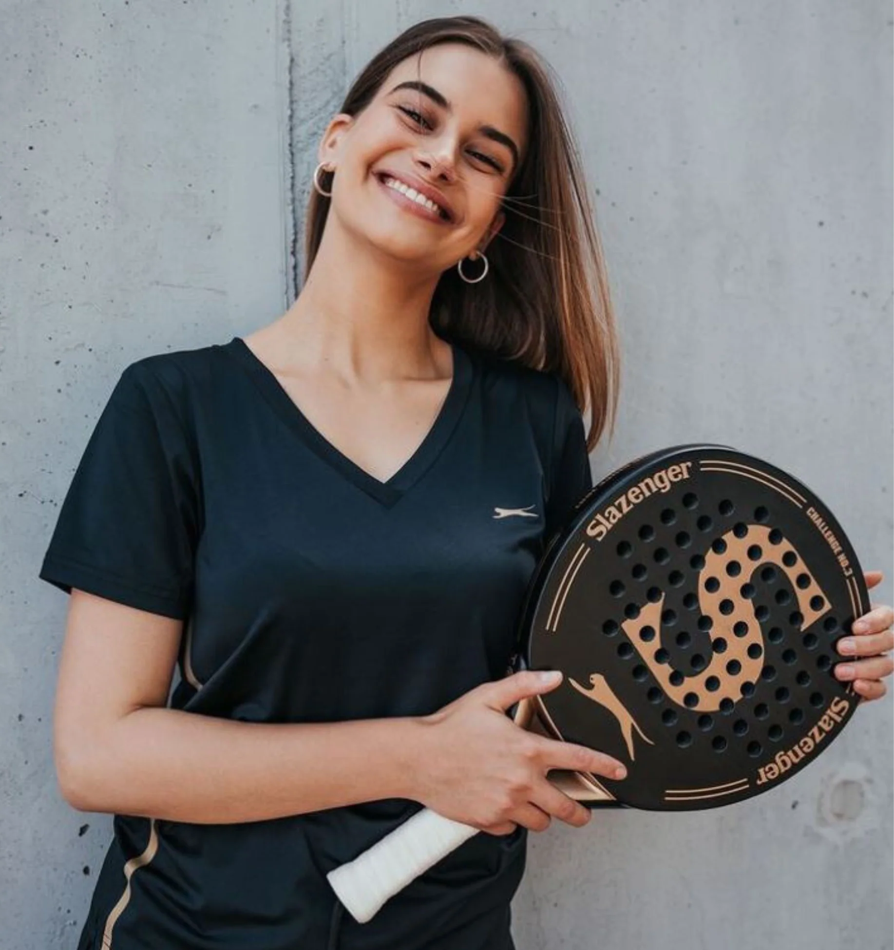 Woman holding a Slazenger paddle against a concrete wall
