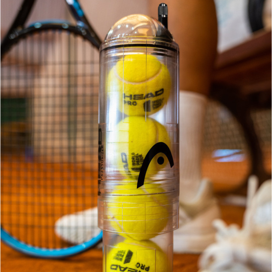 Clear container with tennis balls and a racket in the background